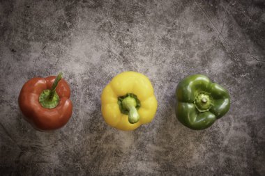 Siyah çimento arka planında kırmızı, sarı ve yeşil çan biberi çeşitleri.