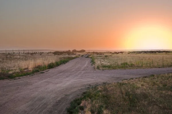 El sol se pone sobre un camino de tierra en la pradera . —  Fotos de Stock