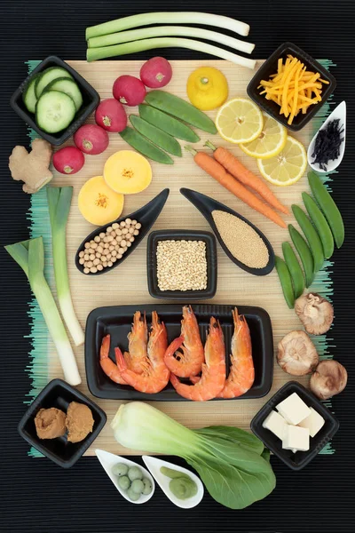 Macrobiotic diet food with seafood, wasabi paste and nuts, tofu, miso, legumes, seaweed, grains, fruit and vegetables with foods high in protein, fiber, antioxidants, minerals and vitamins. On bamboo background, top view.