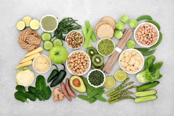 Vegan health food for a healthy life concept with green and cream coloured vegetables, fruit, spice, legumes, noodles, crackers & dips. High in proteins, vitamins, minerals, antioxidants & fibre,