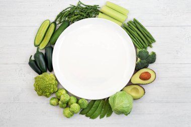 Yeşil sebzeli vegan sağlıklı yiyecek çelengi, kırsal kesimdeki boş bir tabağı çevreleyen bağışıklık sistemini güçlendirmek için. Yüksek vitamin, mineral, antioksidan ve diyet lifleri içeren gıdalar. Etik yemek.
