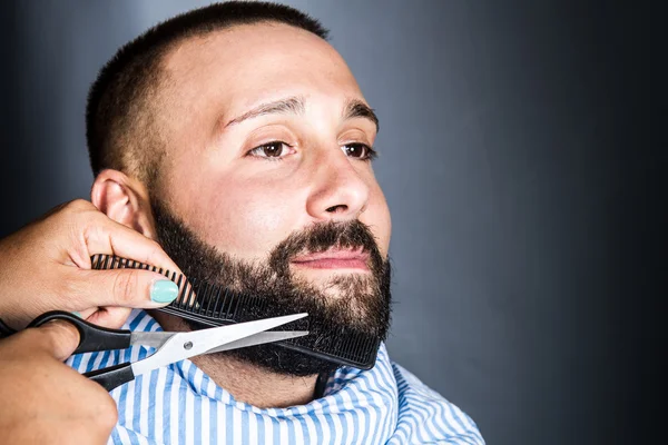 Mujer está cortando la barba de un hombre joven —  Fotos de Stock