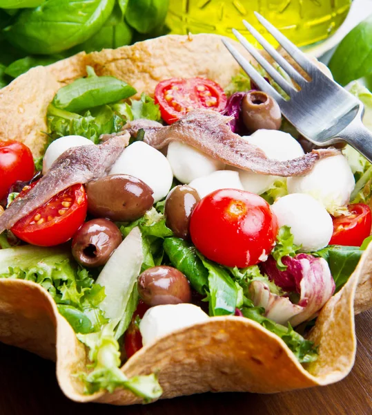 Mixed salad with mozzarella and anchovy in a bread basket — Stock Photo, Image