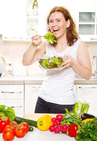 在现代厨房里吃新鲜沙拉的年轻女人笑着 — 图库照片
