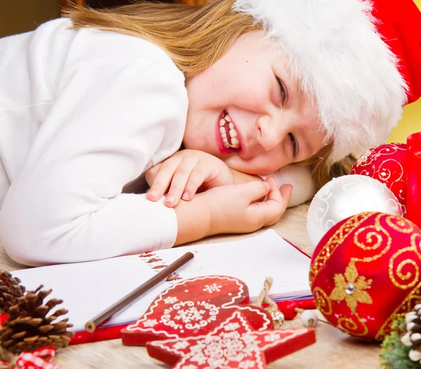 Funny girl in Santa hat writes letter to Santa near christmas de — Stock Photo, Image