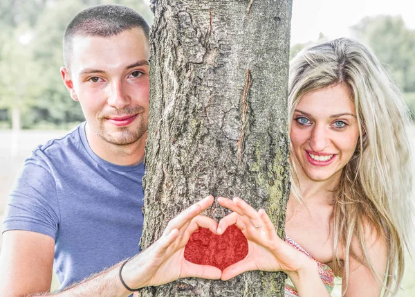 Pareja comprometida en el parque que hacen el símbolo del corazón — Foto de Stock