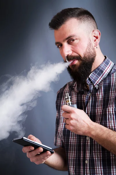 Barbudo hombre fumar cigarrillo electrónico mirando a la smartpho —  Fotos de Stock