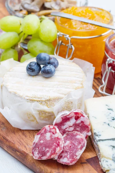 Houten snijplank met kaas, vleeswaren en jam — Stockfoto