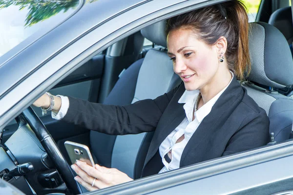 Счастливая женщина в своей новой машине смотрит на мобильный телефон — стоковое фото