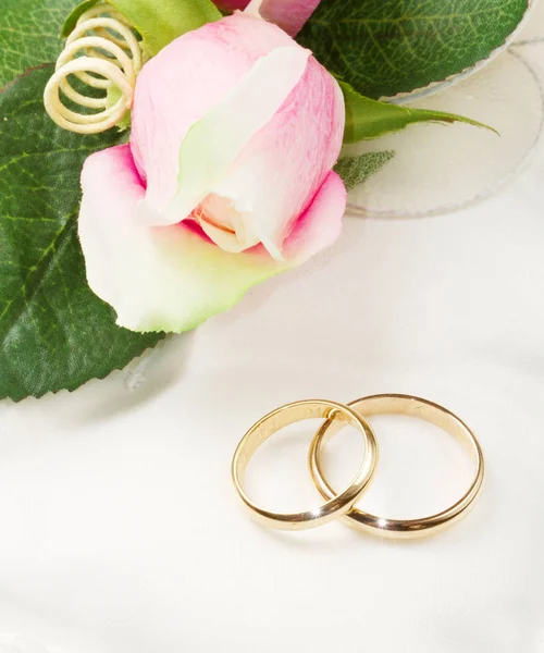 Zlaté snubní prsteny na bílém polštáři s růží — Stock fotografie