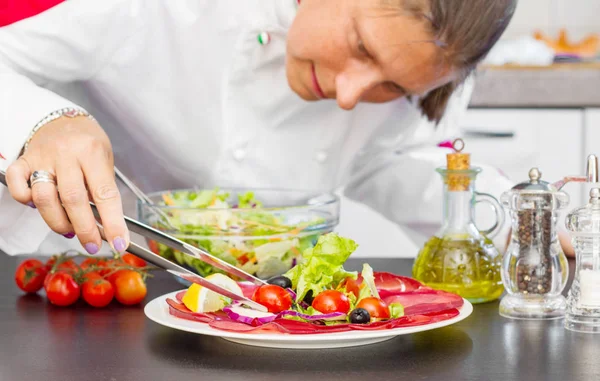 Koki profesional menyiapkan piring dengan salami dan salad segar — Stok Foto