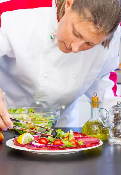 Professionell kock förbereder en tallrik med färsk sallad och salami — Stockfoto