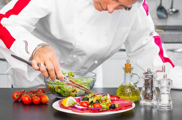 Professionell kock förbereder en tallrik med färsk sallad och salami — Stockfoto