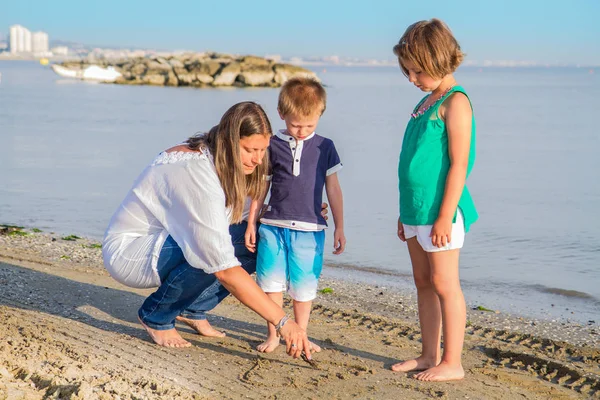 母と彼女の子供たちが砂の上を書く — ストック写真