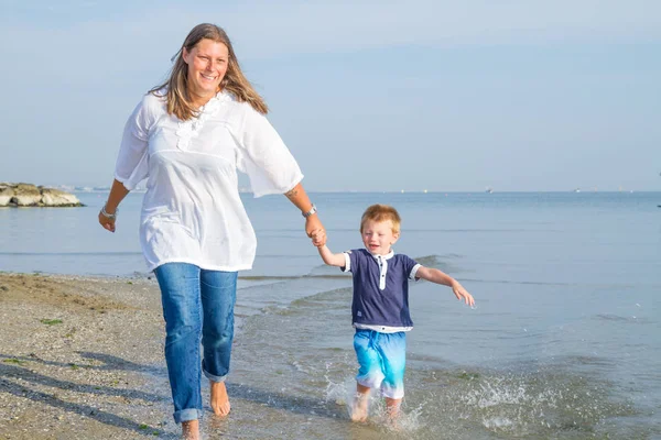 Maman et bébé courent sur le sable près de la mer — Photo