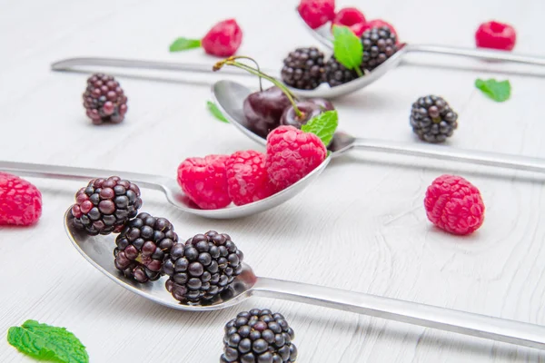 Fresh berries on steel spoons on white marble background — Stock Photo, Image