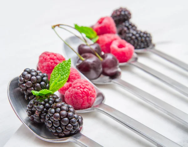 Fresh berries on steel spoons on white marble background — Stock Photo, Image