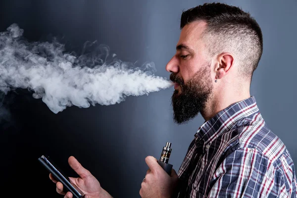 beared man  smoking electronic cigarette looking to the smartpho