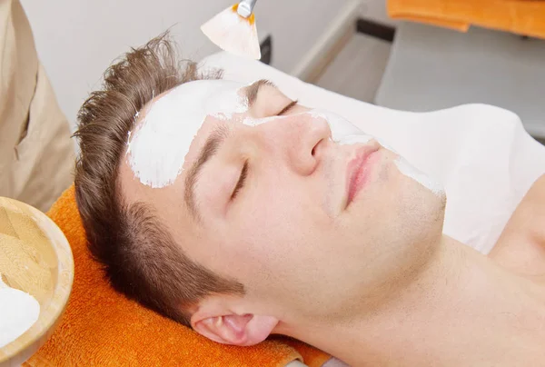 Terapista che applica una maschera per il viso a un bel giovane in una spa — Foto Stock