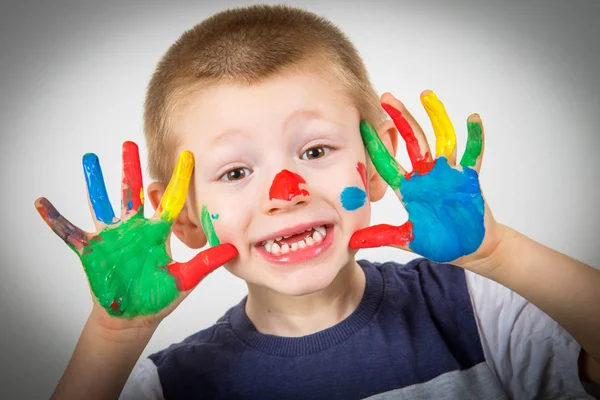 Lächelnder kleiner Junge mit in bunten Farben bemalten Händen — Stockfoto