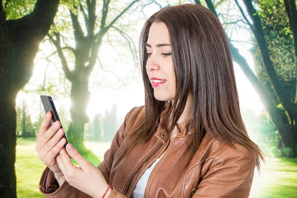 Bella ragazza sorridente guarda il telefono cellulare — Foto Stock