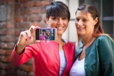 İki arkadaş şehir sokağında selfie çekiyorlar.