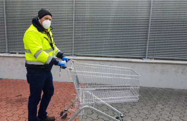 Coronavirus: tıbbi maskeli ve eldivenli bir adam süpermarketten alışveriş arabasıyla bekliyor.