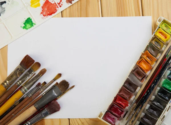 Кисти цветной краски и пустой белой бумаги на деревянный стол — стоковое фото