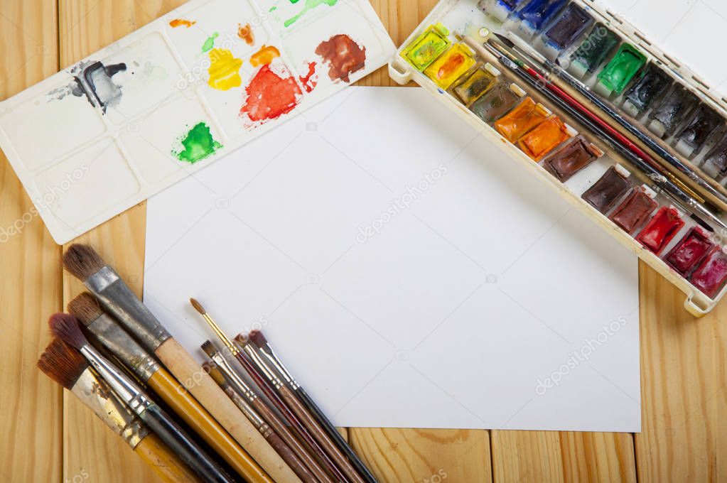 Paint brushes and empty white  paper on a wooden table