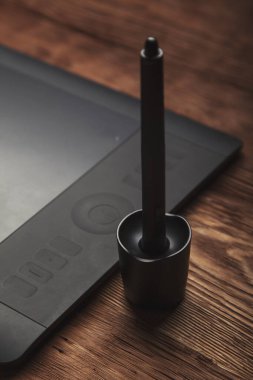 Grafik tablet ve kalemin bir kısmı kahverengi ahşap arka planda yatar.