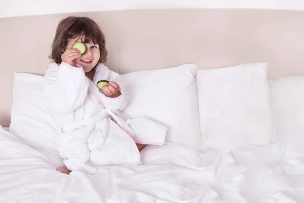 Красивая девушка в халате с нарезанным огурцом на кровати — стоковое фото