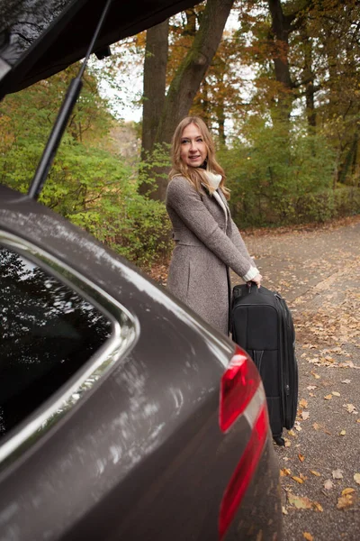 Mulher coloca sua mala no porta-malas do carro — Fotografia de Stock