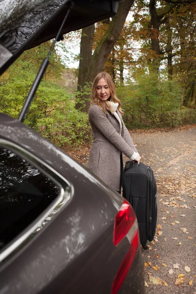 Женщина кладёт чемодан в багажник. Стоковая Картинка