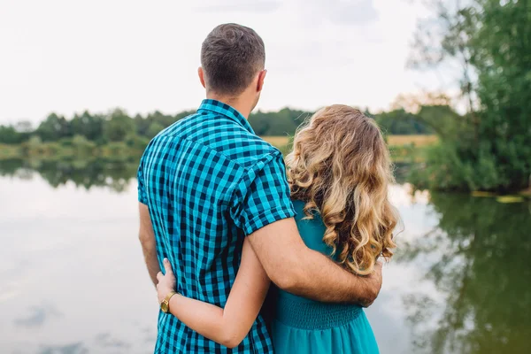 Влюбленная пара, стоящая в стороне и обнимающаяся на фоне озера и природы — стоковое фото