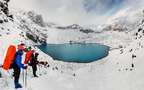 Två turister klättrare i snöiga Kaukasus bergen med utsikt över den blå sjön — Stockfoto