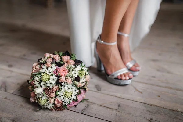 Vrouwelijke voeten in witte bruiloft sandalen met een bruids boeket — Stockfoto