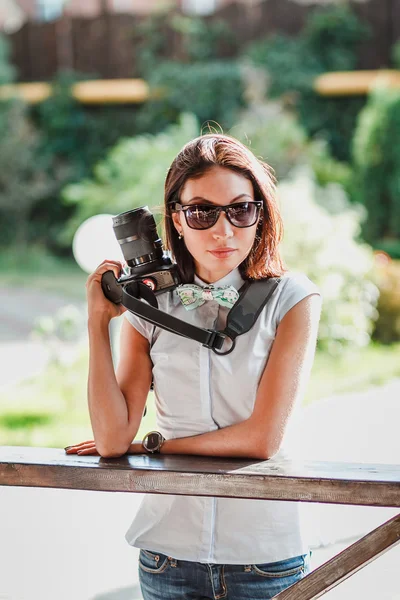 Счастливая молодая женщина в солнечных очках держит современную цифровую фотокамеру — стоковое фото