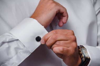 Bir el yakını beyaz gömlek ve kol düğmesi takıyor.