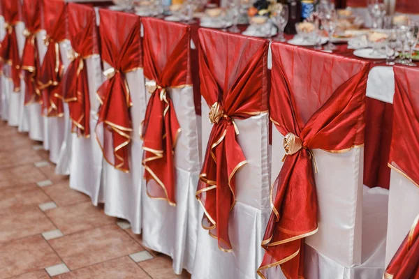 Chaises de mariage en rangée décorées avec un ruban de couleur rouge — Photo