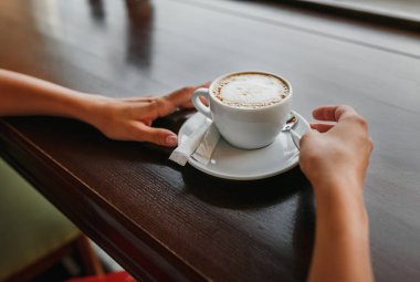 Ahşap doğal masa üzerinde romantik kafede kahve kapuçino deseni ile köpük bardak tutan yakın çekim eller. Renk sıcak tonlu işleme instagram stili.