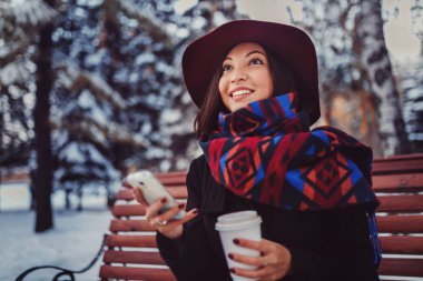 karlı kış parkta bir bankta oturmuş ve sıcak kahve yudumlarken Evet kadın