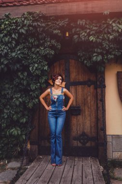 Denim tulum ayakta karşı bir Ivy çerçeveli eski ahşap kapı kale giyen güzel bir kadın portresi. Magical toned
