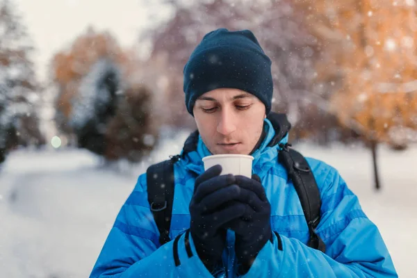 Retrato de um homem vestindo casaco desportivo de inverno azul brilhante e segurando bebida quente em copo de papel descartável takeaway, tiro ao ar livre — Fotografia de Stock