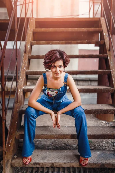 Kentsel genç kadın tonda sit Mavi Jeans acımasız poz, sıradışı demir merdivenlerde atış — Stok fotoğraf