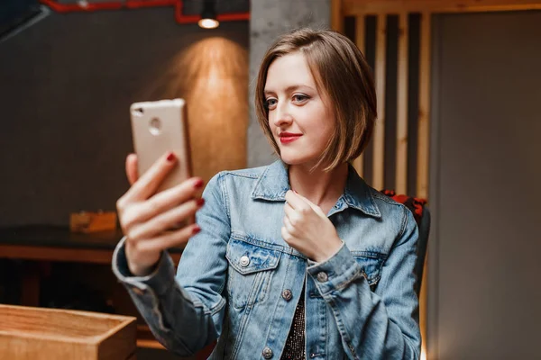 Женщина со смартфоном в ресторане делает селфи и улыбается — стоковое фото