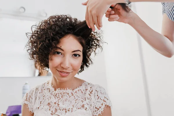 Professional hairdresser artist making curly hairstyle to charming Brunette bride woman with short hair on her wedding day. Beauty Studio interrior — Stock Photo, Image