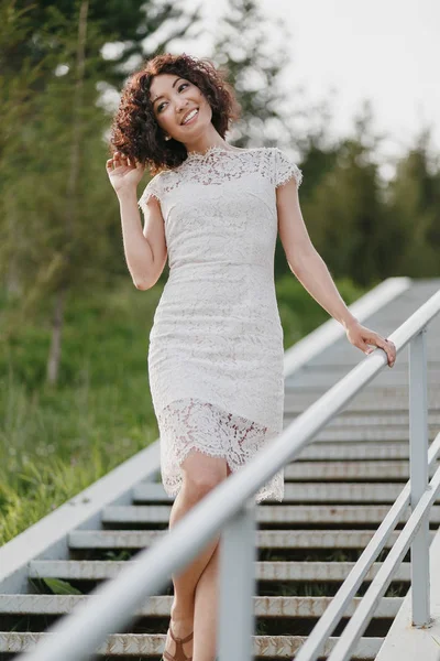 Portrait of a young girl in white lace dress outdoors on a ladder — Stock Photo, Image