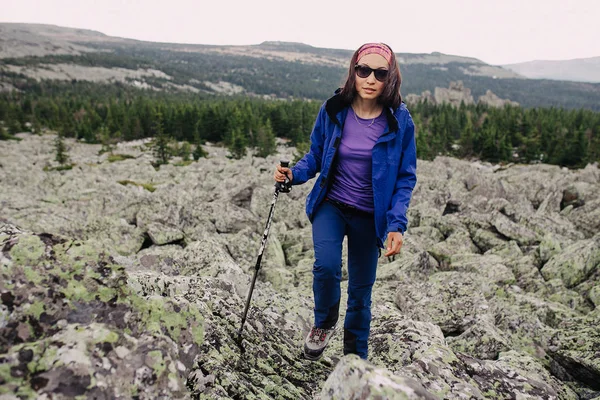 Путешествующая женщина путешествует по горам среди полей из камней и камней. Тропа к высокой вершине — стоковое фото