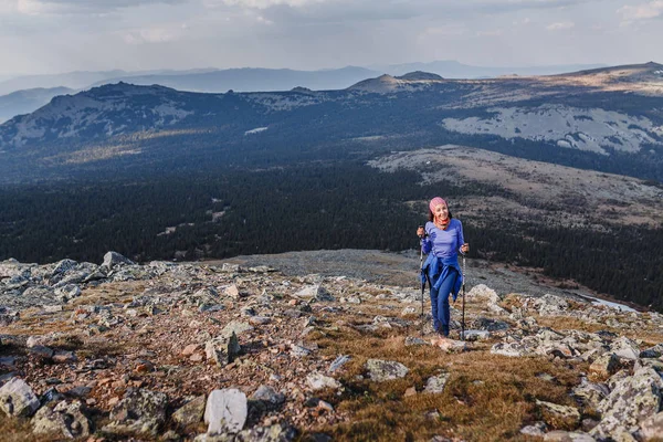 Eine glückliche junge Frau erklimmt den Berg mit einer Trekkingstange. Konzept für einen gesunden und sportlichen Lebensstil. — Stockfoto