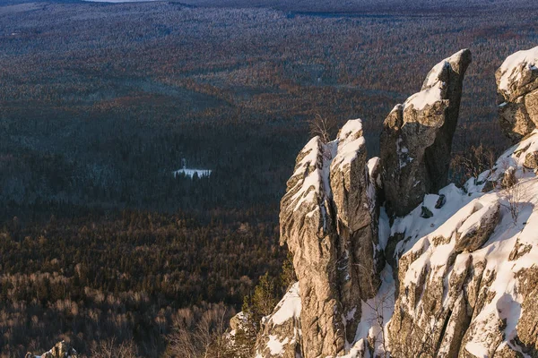 Скалистая вершина базальтовых колонн, покрытая снегом, зимний лес на заднем плане . — стоковое фото
